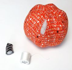 an orange pumpkin sitting next to a spool of thread and a sewing needle on a white surface