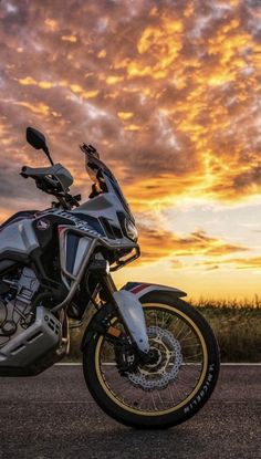 the motorcycle is parked on the side of the road as the sun sets in the background