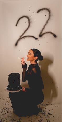 a woman sitting on the floor with a cake in front of her and numbers drawn on the wall behind her