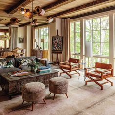 a living room filled with lots of furniture and large windows covered in wooden beams that look out onto the woods