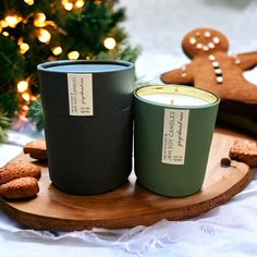 two candles sitting on top of a wooden tray next to cookies and a christmas tree