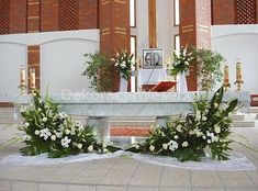 the altar is decorated with white flowers and greenery in front of two rows of windows