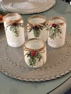 four mason jars decorated with evergreen and red berries are sitting on a place mat next to plates