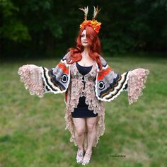 a woman with red hair and wings is standing in the grass