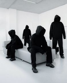 four people in black hoodies sitting on white couches, all facing different directions