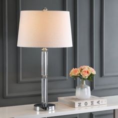 a table with a lamp on top of it next to a book and flower vase