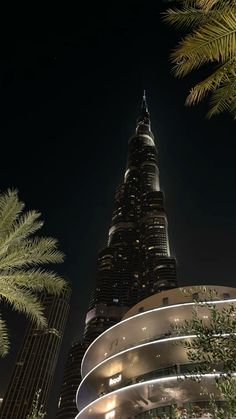 the burj building is lit up at night in front of palm trees and skyscrapers