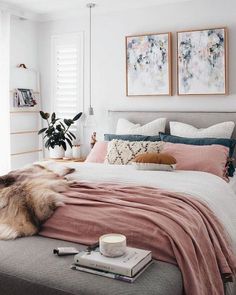 a bed with pink sheets and pillows in a bedroom next to two pictures on the wall