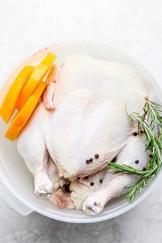 a whole chicken in a plastic container with carrots and rosemary on the side for garnish