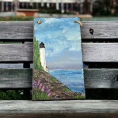 a painting is sitting on a bench by the water and it's light house