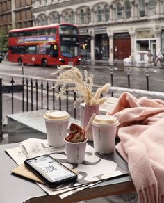 two cups of coffee are sitting on a table in front of a city street with a red double decker bus