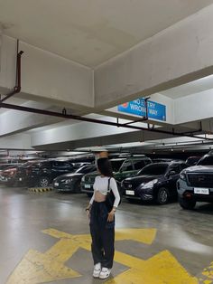 a woman standing in a parking garage next to a yellow star on the floor with cars parked behind her