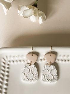 two pairs of earrings sitting on top of a white tray next to a vase with flowers