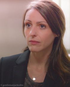 a woman with long hair wearing a black blazer and a gray shirt is looking at the camera