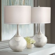 two lamps sitting on top of a white table next to a window with curtains in the background