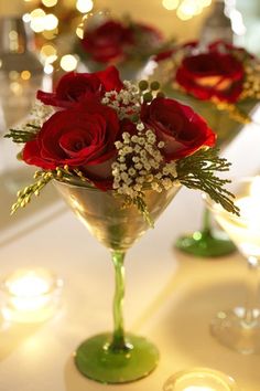 red roses sit in a martini glass on a table with candles and lights behind it