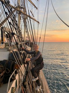 a man standing on the side of a sailboat in the ocean at sunset or dawn