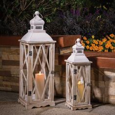 two white lanterns sitting next to each other in front of a planter filled with flowers