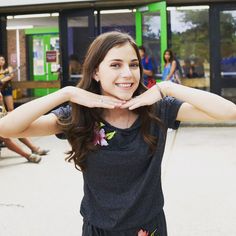 a girl making a heart with her hands while standing in front of a group of people