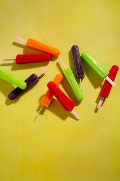 several different colored popsicles on a yellow surface with toothpicks sticking out of them