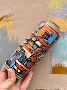 a hand is holding a can with colorful designs on it and the bottom half has been painted