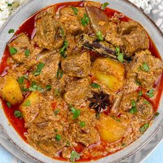 a bowl filled with meat and potatoes covered in sauce next to some rice on a table