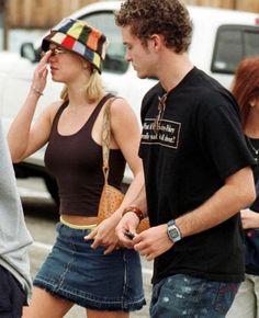 a man and woman walking down the street talking on their cell phones while wearing hats