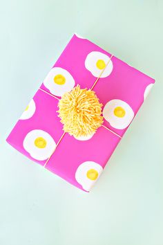 an egg on top of a pink wrapping paper with yellow polka dots and a pom - pom