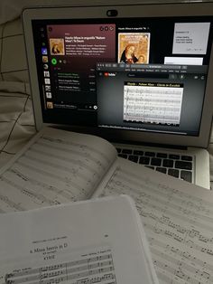 an open book sitting on top of a laptop computer next to sheets of music paper