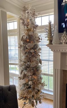 a white christmas tree with silver and gold ornaments on it in front of a fireplace