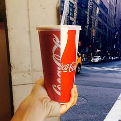 a hand holding up a red cup with a straw in it on the side of a street