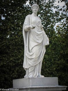 a statue of a woman holding a bowl in her hand and standing next to some trees