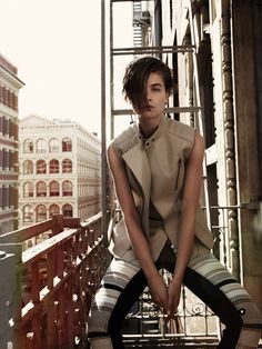 a young man sitting on top of a wooden bench in front of a tall building