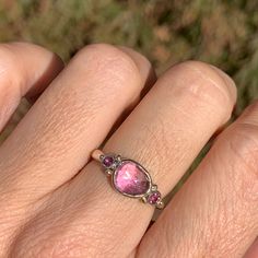 A warm pink sapphire is accented with a pair of burgundy Rhodolite garnets. Set in 14k gold with sterling silver seagrass band we are totally smitten with this ring. Approximate stone size: 9mm x 7mm Approx ct weight: 2cts Mohs Stone Hardness: 9 This one of a kind piece is handmade to order in Emily's Hudson Valley studio. If you have questions about sizing, shipping or need help deciding please reach out to us! Colored Stone Engagement Rings, Stacked Engagement Ring, Rhodolite Garnet Ring, Birthstone Stacking Rings, Peach Sapphire, Pink Sapphire Ring, Sapphire Engagement Ring, Rhodolite Garnet, Stone Engagement Rings