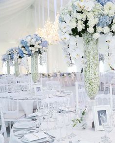 the table is set with white and blue flowers in tall vases on each side