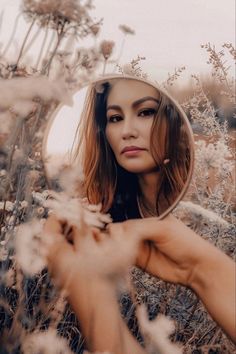 a woman is looking into a mirror in the middle of some tall grass and flowers