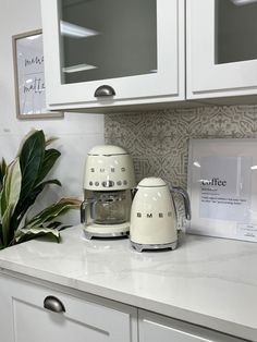 two white appliances sitting on top of a kitchen counter next to a potted plant