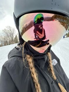 a woman with long hair wearing a helmet and holding a camera in her hand while standing on snow covered ground