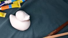 a white plastic duck next to some crayons and paintbrushes on a blue surface