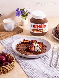 two plates with waffles, ice cream and fruit on them next to a jar of nutella