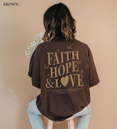 "Introducing our 'Faith Hope Love Shirt,' a Christian Crewneck featuring a bold back print of the uplifting 1 Corinthians 13:13 verse - 'So now faith, hope, and love abide, these three; but the greatest of these is love.' The front chest carries a subtle touch with the words 'Faith, Hope, and Love,' making it an ideal Christian streetwear and a thoughtful gift for Christian girls, daughters, wives, and yourself. Embrace faith-based style with this butterfly-themed tee, embodying Christian values in every thread. #FaithHopeLoveShirt #ChristianStreetwear #GiftsForHer * Q U I C K * F A C T S * ✺ 100% preshrunk cotton ✺ Wash (inside out) and dry normally (on cool for best results) * S I Z I N G * ✺ Sizing is unisex so runs like men's, though not overly large ✺ Most women find their typical siz Inspirational Crew Neck Tops With Letter Print, Inspirational Short Sleeve Tops With Letter Print, Inspirational Graphic Print T-shirt For Fall, Inspirational Graphic Print Crew Neck Top, Inspirational Text Print Relaxed Fit Top, Inspirational Text Print Tops With Relaxed Fit, Inspirational Text Print Tops In Relaxed Fit, Inspirational Text Print Top With Relaxed Fit, Relaxed Fit Inspirational Slogan Tops