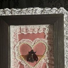 a bee in a heart frame with lace on the edge and an insect attached to it