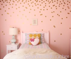 a pink bedroom with gold polka dots on the wall and a white bed in front of it