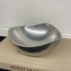 a silver bowl sitting on top of a book next to a white wall and floor