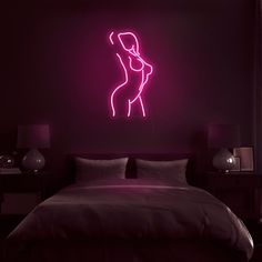 a neon sign above a bed in a dark room with a woman's body on the wall