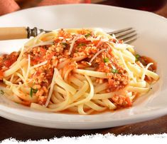 a white plate topped with pasta and sauce next to a fork on a wooden table