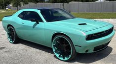 a light blue car parked in a parking lot next to a fence and green grass