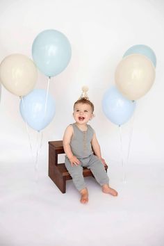 a baby sitting on a stool with balloons in the air