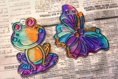 two colorful frog magnets sitting on top of a newspaper