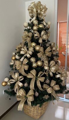 a small christmas tree with gold ornaments in a basket on the floor next to a window